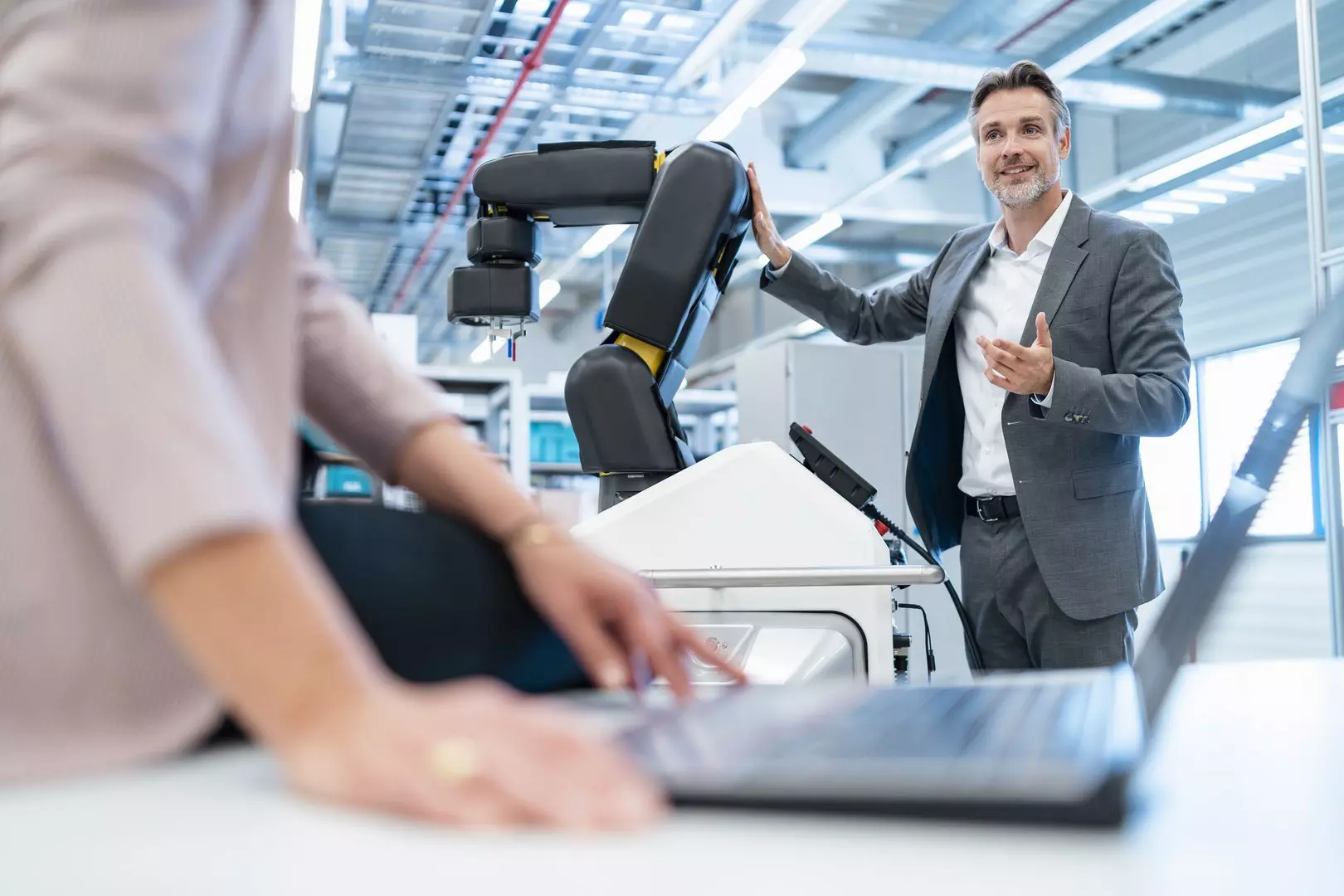 Businessman and businesswoman with laptop and robot in a modern factory hall